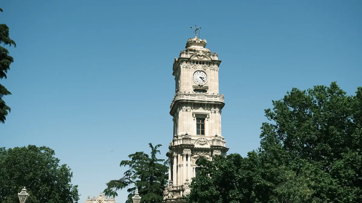 A historic clock tower stands tall amidst lush greenery and blue skies.
