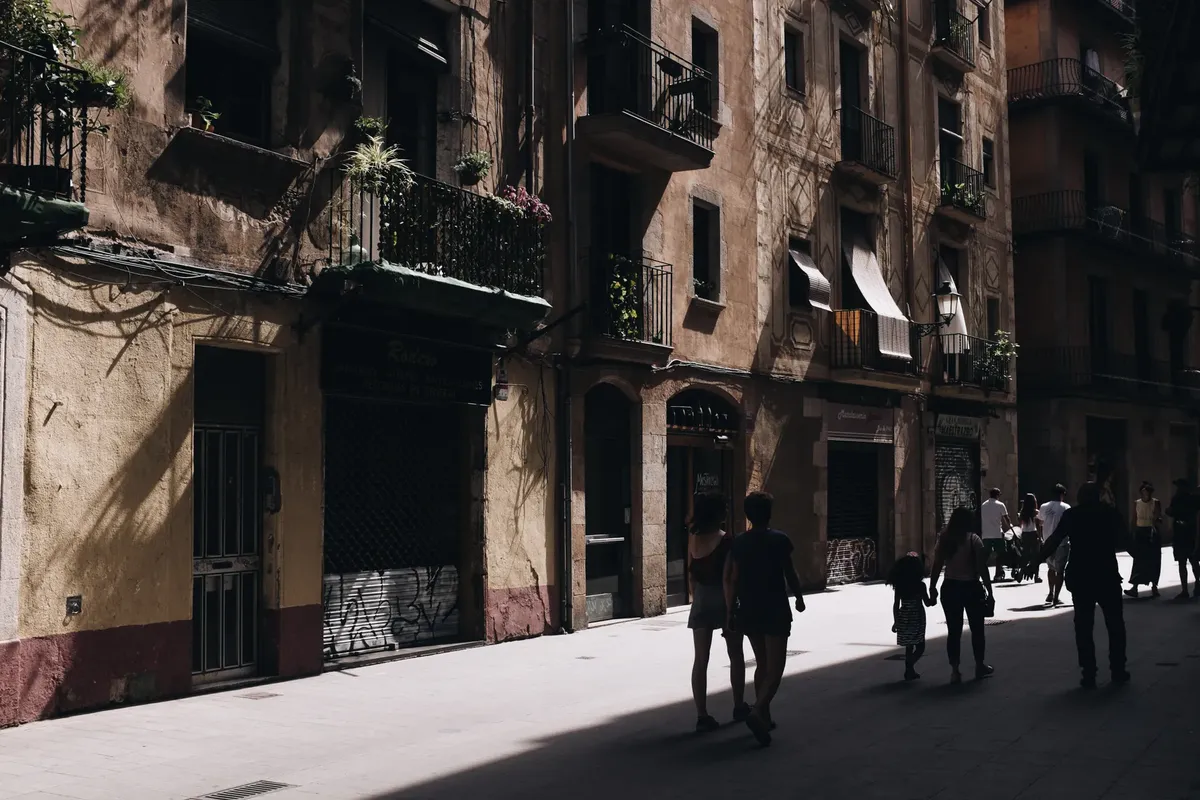 A bustling urban street in Barcelona with historical architecture and shadow play on the facades.