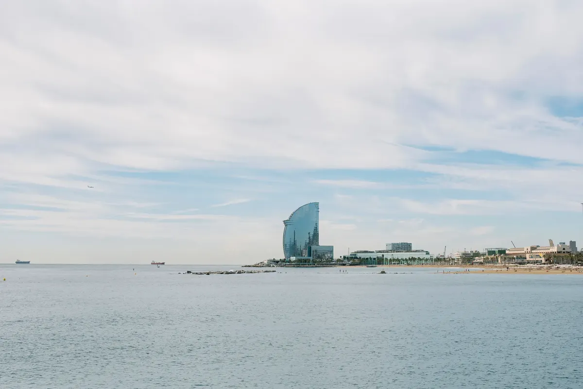 Serene coastal view of W Barcelona Hotel with calm sea and city skyline in the background.